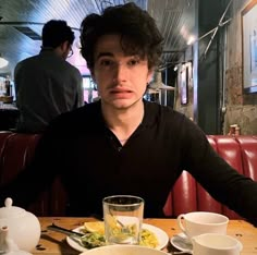 a young man sitting at a table with food and drinks in front of him,