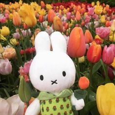 a stuffed rabbit is standing in a field of tulips and other colorful flowers