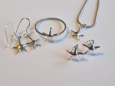 Discover the enchantment of the ocean with this exquisite starfish jewelry set, crafted to capture the wonder of the sea. This set includes a delicate necklace, a stylish ring, a pair of elegant stud earrings, and a pair of dangling earrings, all featuring the iconic starfish design. Each piece is finely crafted from high-quality silver, showcasing the intricate details of the starfish's arms and texture. The necklace's pendant gracefully hangs from a sleek silver chain, while the ring's twisted Ocean-inspired Jewelry With Star Charm, Adjustable Starfish Charm Jewelry, Elegant Starfish Charm Jewelry For Gifts, Elegant Starfish Charm Jewelry As Gift, Elegant Starfish Charm Jewelry Gift, Adjustable Star-shaped Jewelry With Starfish Charm, Starfish Shaped Jewelry With Star Charm As Gift, Ocean-inspired Sterling Silver Jewelry For Anniversary, Elegant Sterling Silver Jewelry With Starfish Charm