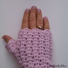 a woman's hand wearing a pink crocheted mitt on top of a white surface