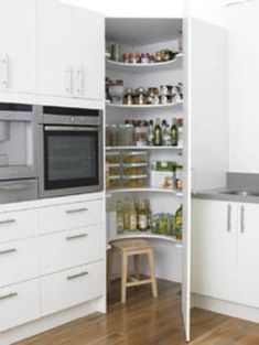 an open pantry in the middle of a kitchen with white cabinets and wood flooring