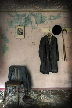 an old room with a chair and coat hanging up on the wall next to a hat rack