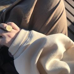 a person sitting on a bench wearing a white sweater and holding a small gold ring