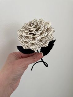 a person holding up a flower made out of old book pages with black leaves on it