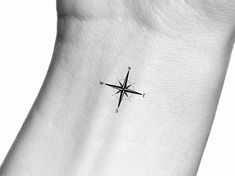 a black and white photo of a small compass tattoo on the left side of the wrist