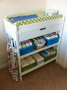 a white baby changing table with green and white polka dots on the top, next to a blue basket filled with diapers