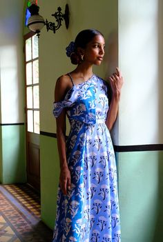 a woman in a blue and white dress leaning against a wall