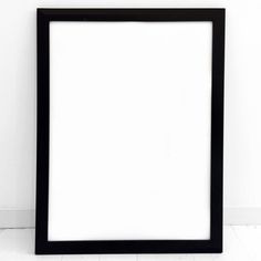 a black frame sitting on the floor in front of a white wall