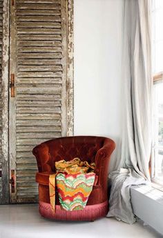 a chair sitting in front of a window next to a wooden door with shutters