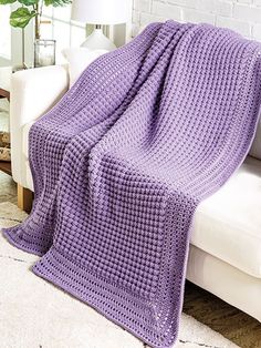 a purple crochet blanket sitting on top of a white couch