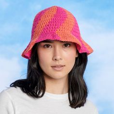 a woman wearing a pink and orange crochet hat with long black hair in front of a blue sky