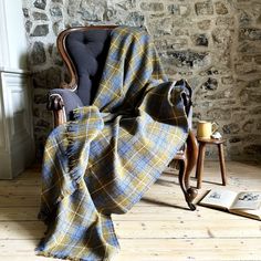 a chair with a plaid blanket on it next to an open book and coffee cup