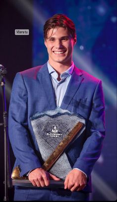 a man in a blue suit holding an award on stage with a microphone behind him