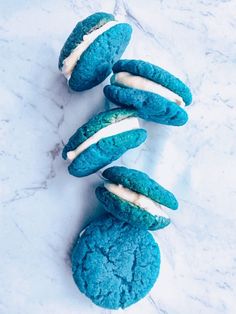 four blue cookies with white frosting on them sitting on a marble counter top next to each other