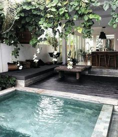 an indoor swimming pool surrounded by greenery and wooden decking, with seating area next to it