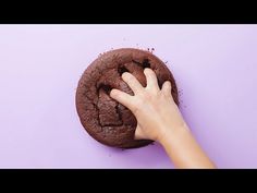 a hand touching a chocolate cookie on a purple surface