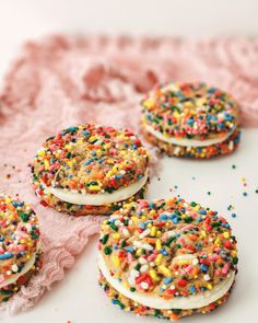 four cookies with sprinkles and white frosting are on a pink doily