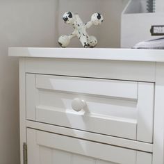 a toy dog sitting on top of a white dresser next to a drawer with drawers