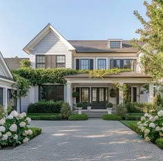 a large white house with lots of windows and bushes in front of it, along with flowers on either side of the driveway