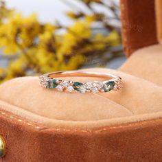 an emerald and diamond ring sitting on top of a velvet box with flowers in the background