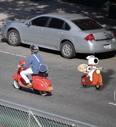 two people on scooters driving down the street in front of a parked car