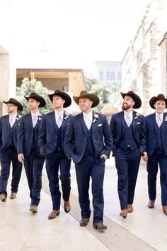 a group of men in suits and hats walk down the street together wearing cowboy hats