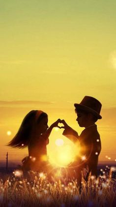 two children making a heart shape with their hands in front of the sun at sunset