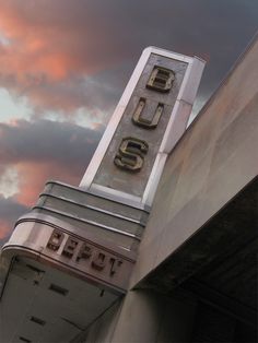 an old theater sign on the side of a building with clouds in the sky behind it