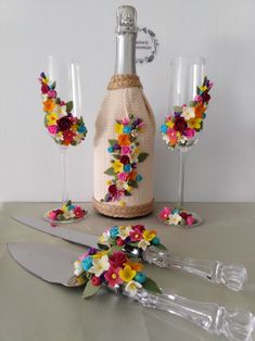 a bottle with flowers on it next to two wine glasses and a silverware holder