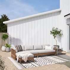 a couch sitting on top of a rug next to a white building with potted plants