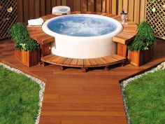 a hot tub sitting on top of a wooden deck next to a green lawn and fence