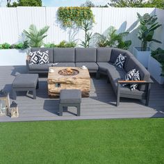 an outdoor living area with couches, tables and plants on the decking in front of a white fence