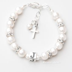 This classic white crystal pearl and sparkling rhinestone bracelet is a suitable gift for a baby girl's baptism, a flower girl, or for a girl celebrating her first Holy Communion. It may be personalized with one solid sterling silver letter bead. - Dainty, 6mm white crystal pearls are punctuated by rhinestone rondelles The number of pearls and rhinestones will vary based on the size. (Not a rosary bracelet.) - A hand-wrapped, sweet white crystal pearl and a small solid sterling silver cross adorn the end of the sterling silver extender chain. - The 1-inch, attached sterling extender chain allows for flexibility in sizing and room for a little growth so the bracelet may be worn for a longer period of time. - Constructed with professional-grade jewelry wire and finished with sterling silver White Name Bracelets For Wedding, Classic Personalized White Pearl Bracelet, Personalized White Bracelets For Wedding, White Hypoallergenic Pearl Bracelet For First Communion, Hypoallergenic White Pearl Bracelet For First Communion, Elegant Beaded Jewelry For Baptism, Elegant White Name Bracelets, Personalized White Pearl Bracelet For Baptism, White Pearl Charm Bracelet For First Communion