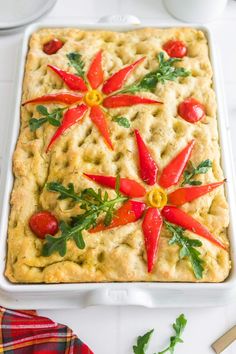 a square casserole with red peppers and green leaves on top, sitting on a white surface