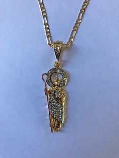 "St. Judas 14k Plated Gold and Crystal Necklace. Made in Mexico// San Judas Tadeo 14k chapeado en oro diamantado con cristales blanco transparente y cadena Hecho en Mexico Pendant measurement: 4cm //Medida del dije: 4cm Weight: 0.2 oz (7 grams) //Peso: 0.2 oz (7gramos) Necklace measurement: 24¨inches, 2mm anchor//Medida de la cadena: 24\" pulgadas, 2mm anchor Weight: 0.1 oz (5 grams) //Peso: 0.1 oz (5 gramos)" Gold Cubic Zirconia Necklace With Figaro Chain, Diamond Figaro Chain Jewelry As Gift, Spiritual Gold Jewelry With Diamond Cut, 14k Gold Jewelry With Bling, Gold Bling Pendant Jewelry, Gold Spiritual Jewelry With Diamond Cut, Spiritual Gold Diamond Cut Jewelry, Gold Spiritual Necklace With Diamond Accents, Figaro Necklace