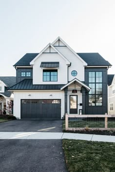 a large white and black house with two garages on each side of the driveway