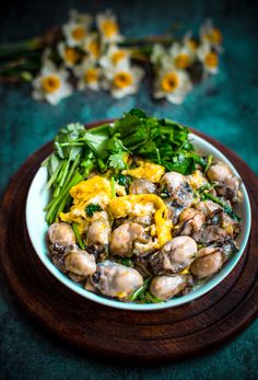 a white bowl filled with mushrooms and greens on top of a wooden table next to flowers