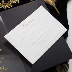 a black and white wedding card with gold foil on the inside is laying next to a feather