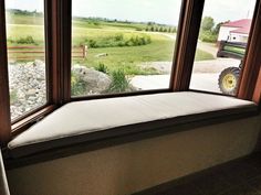 a window seat in front of a large window with the view of a farm field