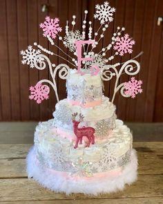 a three tiered cake decorated with pink and silver frosting, snowflakes and a deer