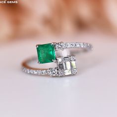 an emerald and diamond ring sitting on top of a table