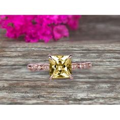 a yellow and white diamond ring sitting on top of a wooden table next to pink flowers