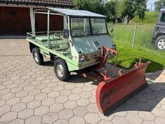 an old green utility vehicle with a snow plow attached to the front and side