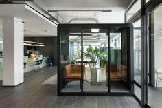 an office with glass walls and doors leading to the meeting room, while people sit at desks