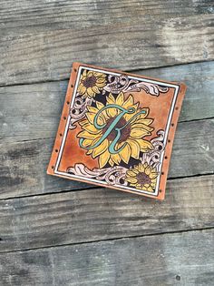 a leather wallet with sunflowers on it sitting on a wooden table next to a pair of scissors