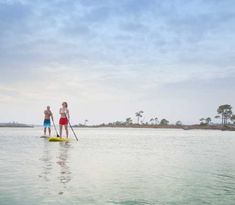 two people standing on surfboards in the water with paddles and poles attached to their backs