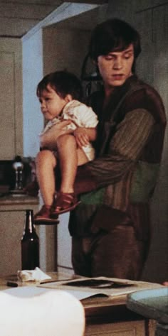 a man holding a baby in his arms while standing next to a kitchen counter top