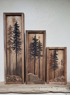 three wooden framed pictures with trees painted on them in different sizes and shapes, sitting on a shelf