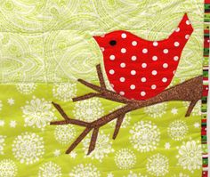 a red bird sitting on top of a green and white quilted wallhange