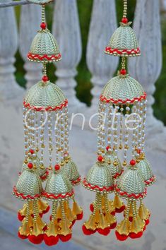 three bells hanging from the side of a wooden fence with red beads and gold trimmings